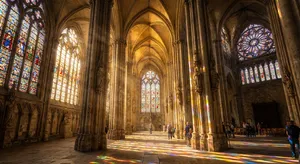 A Gothic cathedral interior at sunset with light streaming through detailed stained glass windows, creating colored patterns on stone floors and columns. Show accurate ribbed vaulting. - Google Nano Banana Pro
