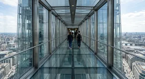 Photorealistic rendering of a contemporary glass skybridge between two skyscrapers, seen from inside with city views visible through glass walls and floor. Show accurate reflections and structural details. - Takumi Takumi 1