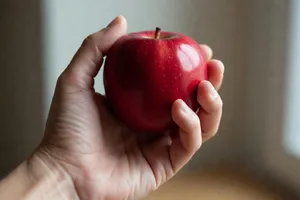 A realistic photo of a hand holding a red apple, with all fingers clearly visible. - XAI Grok Imagine